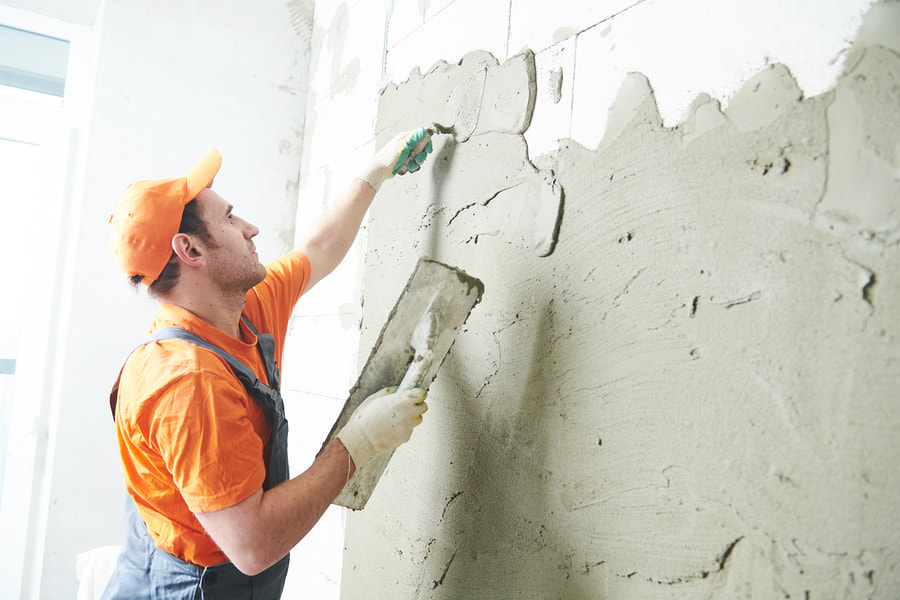 man applying first rough coat of cement to wall