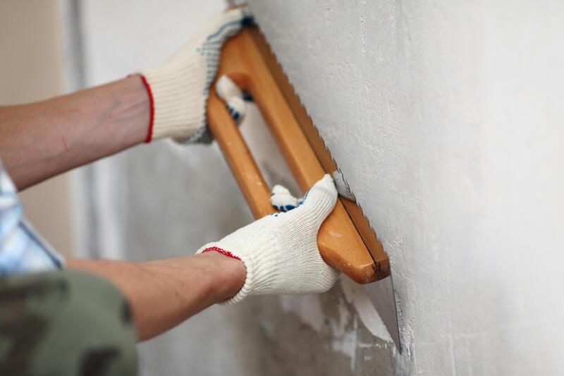 man smoothing cement on wall with wood handled tool