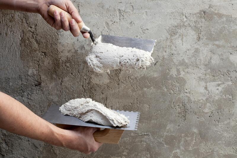 man applying stucco to wall with two metal tools